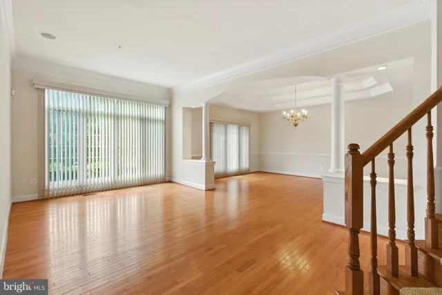 an empty room with wooden floor chandelier and windows