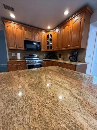 a kitchen with stainless steel appliances kitchen island granite countertop a refrigerator stove top oven and sink