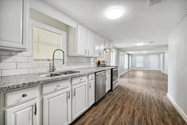 a kitchen with granite countertop white cabinets a sink a window and stainless steel appliances