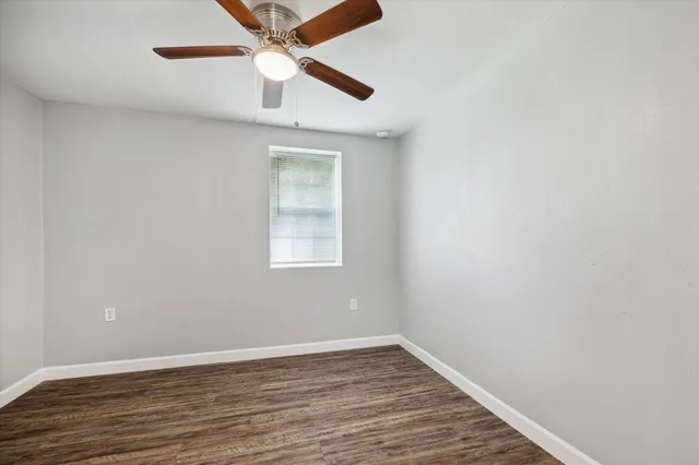 an empty room with wooden floor ceiling fan and window