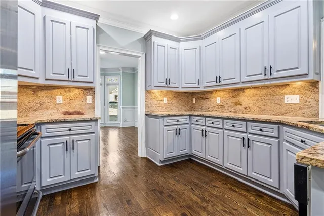 a kitchen with stainless steel appliances granite countertop a stove a sink and white cabinets with wooden floor