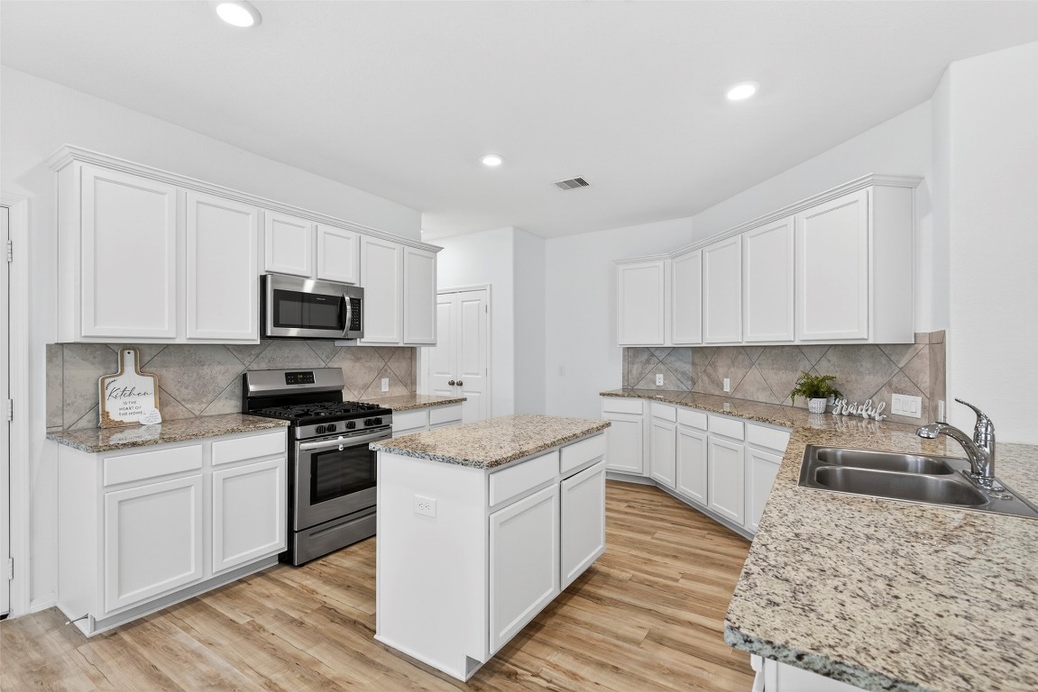 5402 Still Creek Ranch Drive Richmond, TX 77469 - Photo 15 of 32 a kitchen with stainless steel appliances granite countertop a stove top oven a sink dishwasher and white cabinets with wooden floor