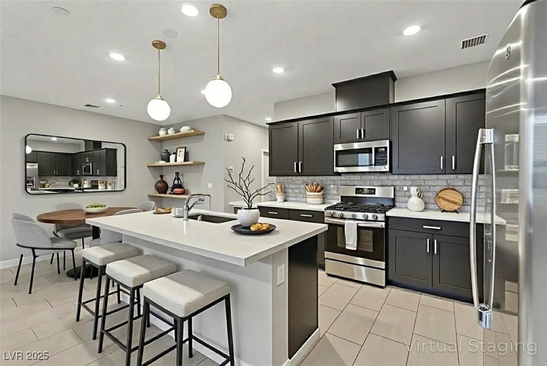 143 Aqua Commons Lane Henderson, NV 89015 - Photo 6 of 20 Kitchen featuring appliances with stainless steel finishes, an island with sink, pendant lighting, a kitchen bar, and light tile patterned floors