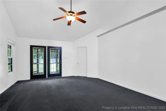 an empty room with chandelier fan and windows