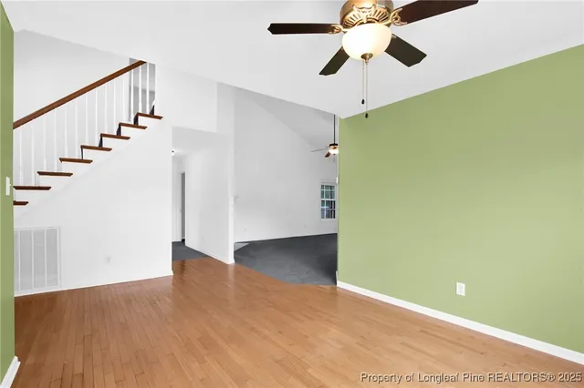 a view of an empty room with wooden floor and a ceiling fan