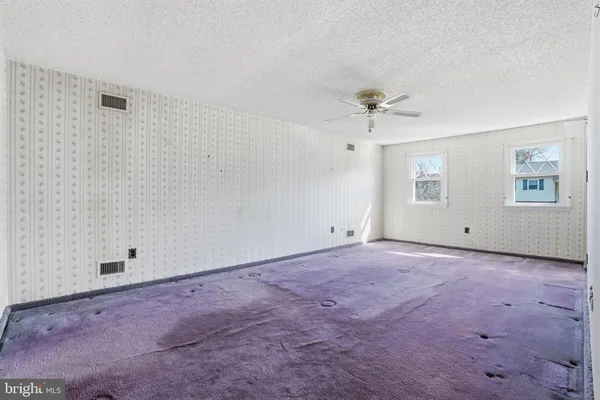 an empty room with chandelier fan and windows