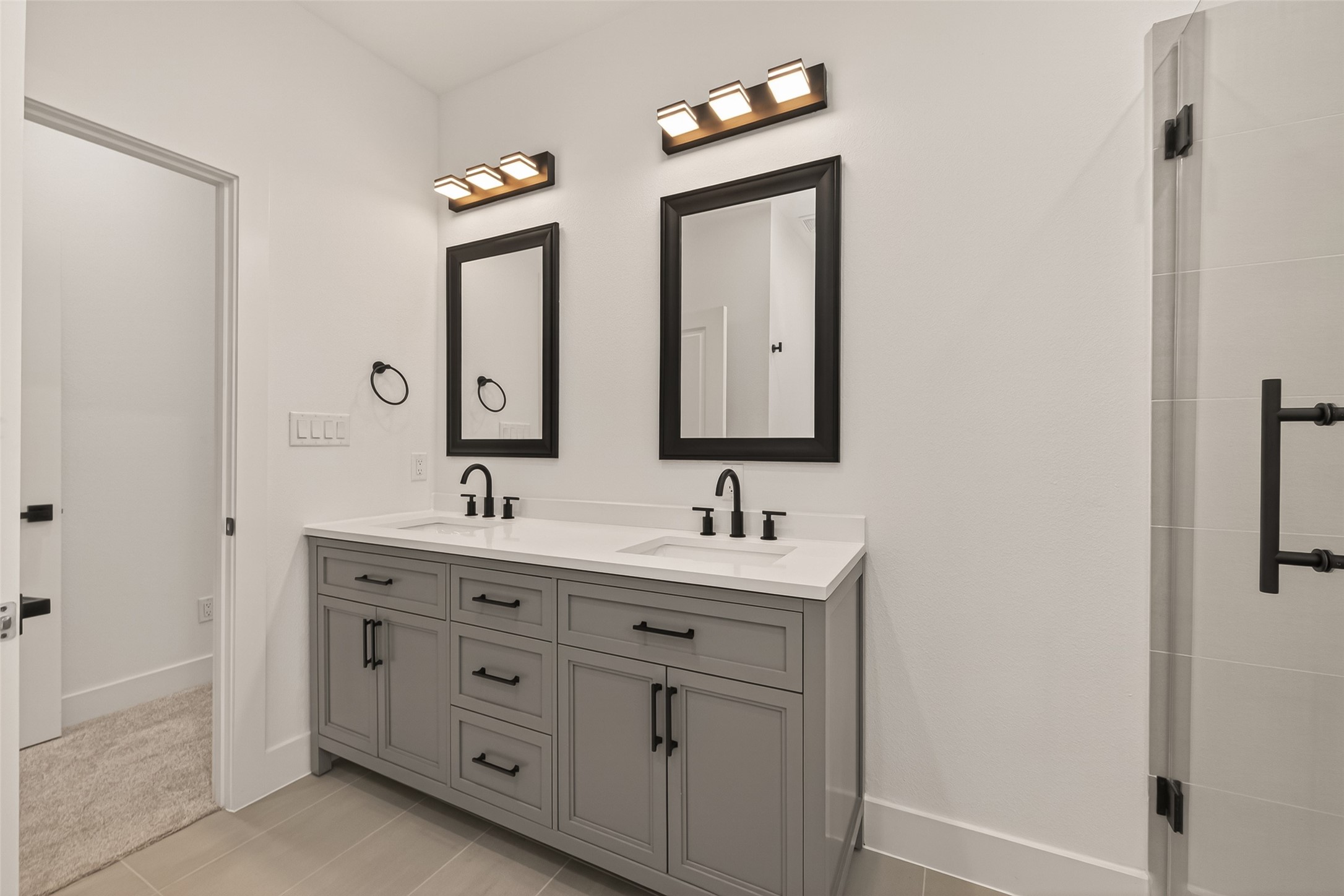 6808 Madrid Street Houston, TX 77021 - Photo 28 of 31 This bathroom features a modern double vanity with sleek black fixtures, framed mirrors, and ample storage. The neutral tones and contemporary lighting create a bright, clean, and stylish atmosphere.