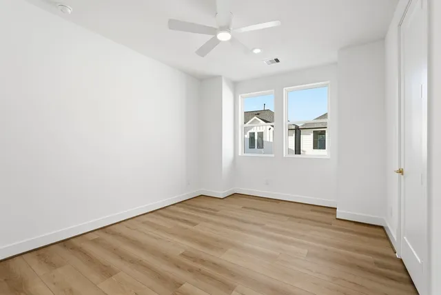 a view of empty room with wooden floor and fan