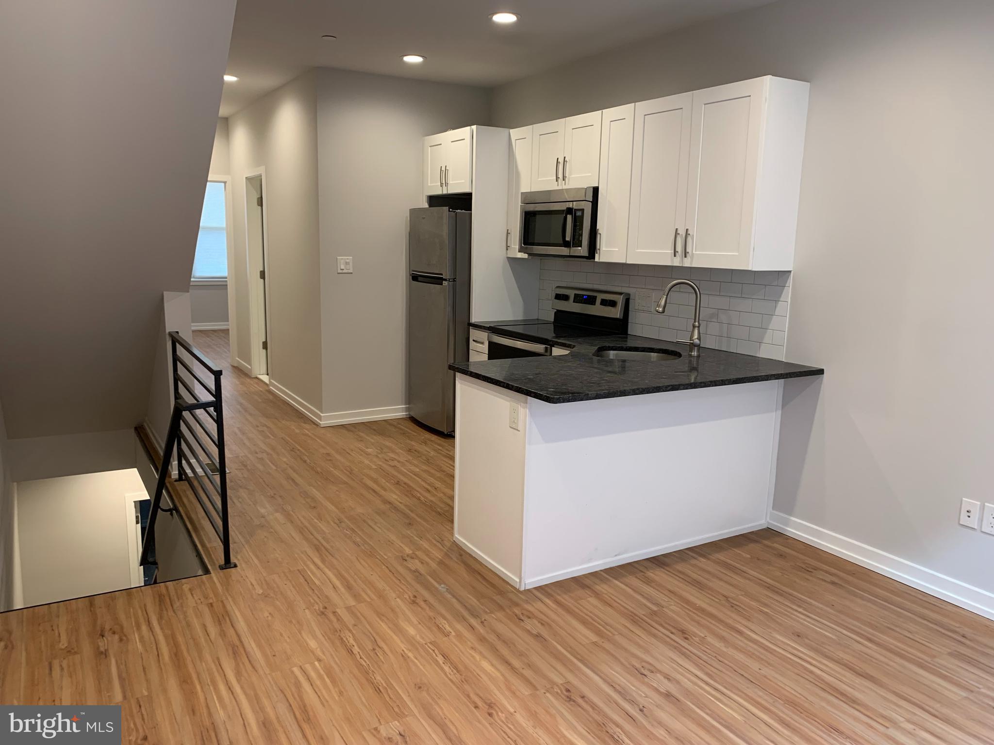 1268 South 27th Street, Unit 1 Philadelphia, PA 19146 - Photo 3 of 26 a kitchen with wooden floor white cabinets and stainless steel appliances