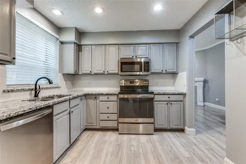 a kitchen with stainless steel appliances granite countertop a stove a sink dishwasher a refrigerator and a microwave oven with wooden floor