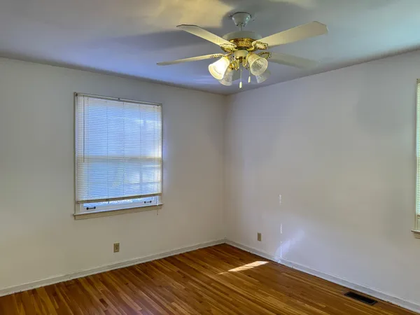 an empty room with a chandelier fan and wooden floor