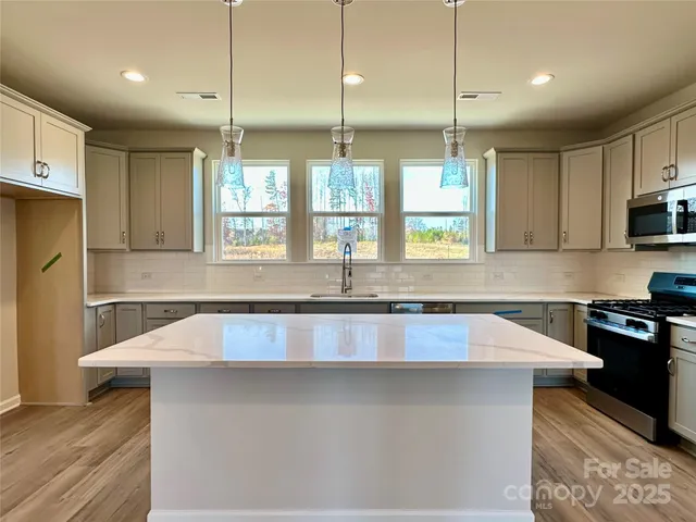 a kitchen with stainless steel appliances a sink a stove a refrigerator a center island a counter space and a window