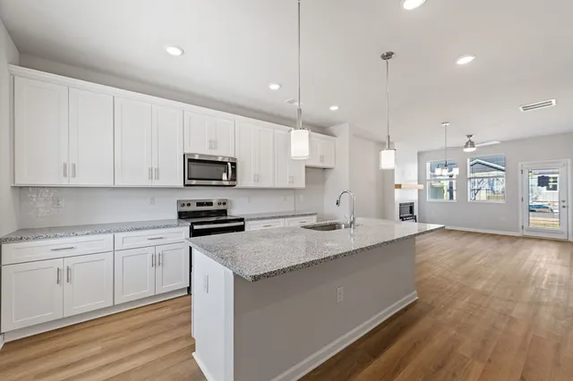 a kitchen with stainless steel appliances granite countertop a sink dishwasher a stove and a refrigerator with wooden floor