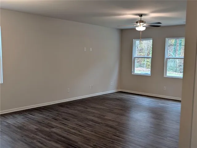 an empty room with wooden floor chandelier fan and windows