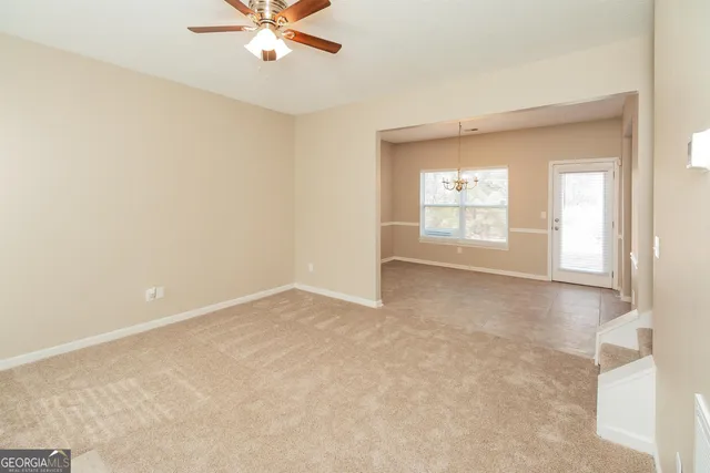 an empty room with chandelier fan and windows