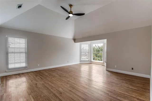 an empty room with wooden floor fan and windows