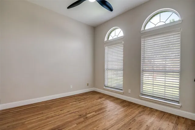 an empty room with wooden floor fan and windows