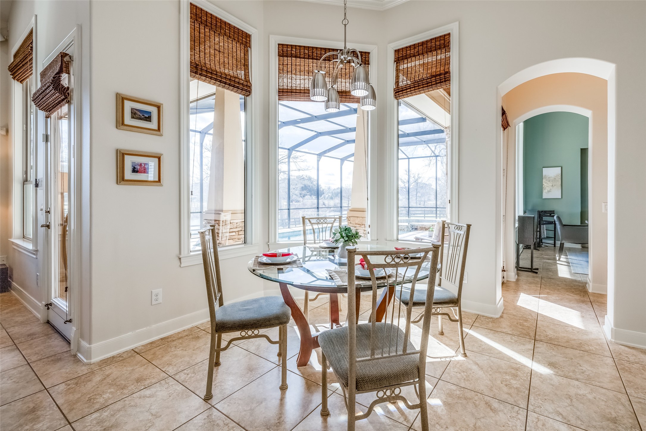 31102 Lower Oxbow Trace Fulshear, TX 77441 - Photo 15 of 50 Breakfast room with door to left out to out to pool, wall of windows, tiled floor, chandelier, arch through to dining room & another door out to pool