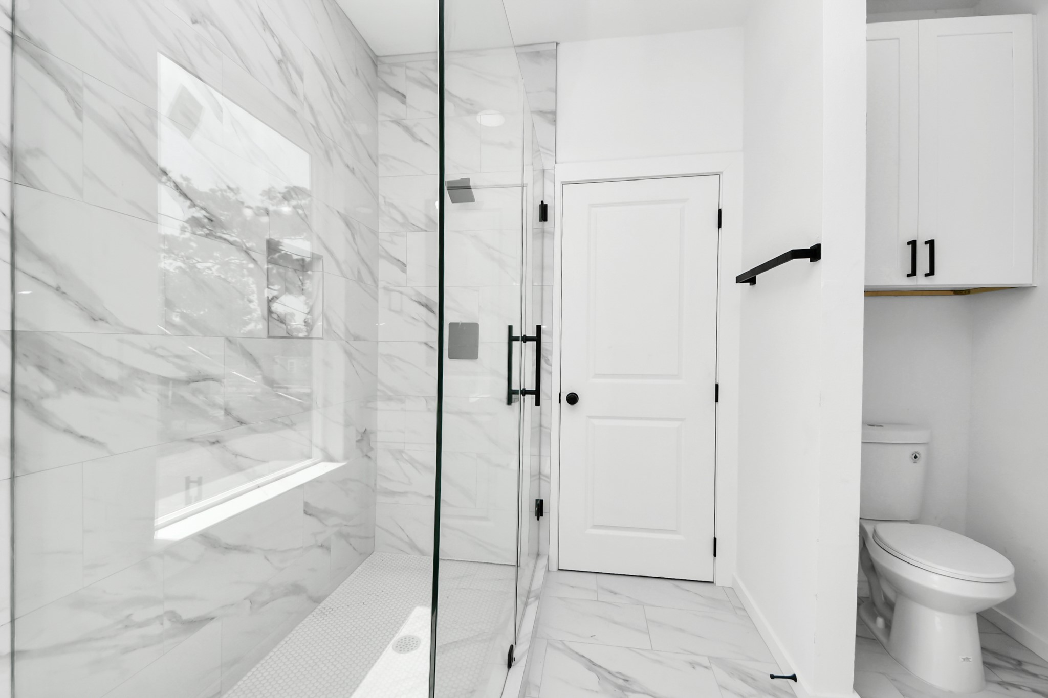 8023 Brandon Street Houston, TX 77051 - Photo 7 of 10 This bathroom features a modern design with a spacious glass-enclosed shower, elegant marble-style tiles, and sleek black fixtures. It includes a toilet and storage cabinets, offering both style and functionality.