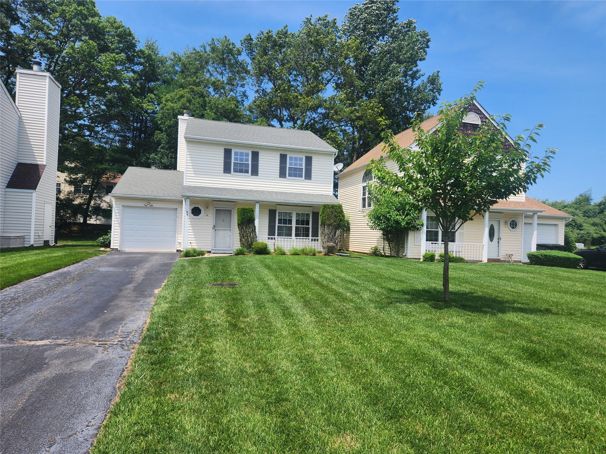 Traditional-style house with asphalt driveway, an attached garage, a front lawn, and covered porch
