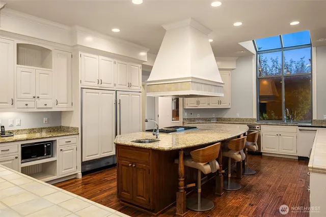 a kitchen with kitchen island granite countertop a stove a sink a refrigerator and white cabinets with wooden floor