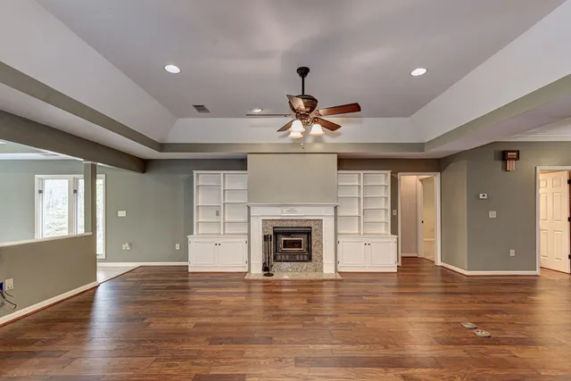 an empty room with wooden floor fireplace and windows
