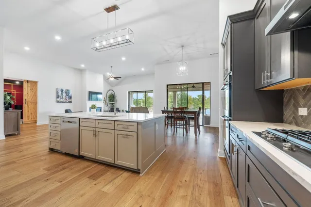 a kitchen with stainless steel appliances granite countertop a stove top oven a refrigerator a dining table and chairs with wooden floor