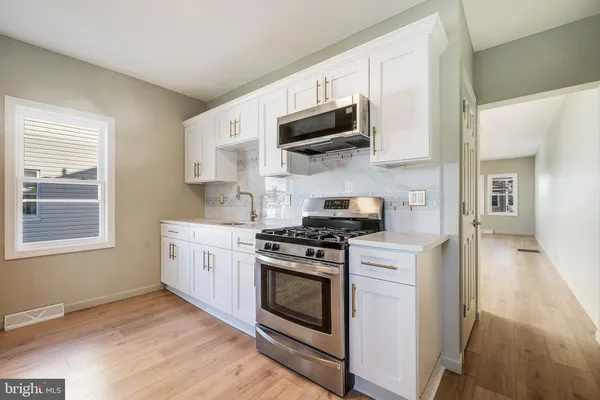 a kitchen with stainless steel appliances white cabinets a sink a stove a microwave and wooden floors