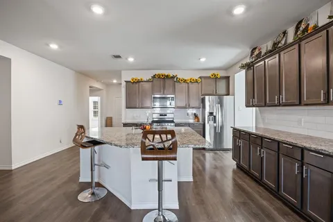 a kitchen with stainless steel appliances granite countertop a stove top oven a sink a refrigerator and white cabinets with wooden floor