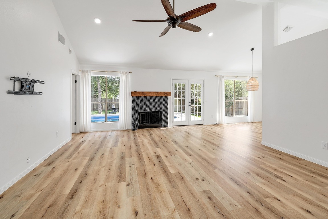 1205 Rambling Trail Cedar Park, TX 78613 - Photo 6 of 38 Open and airy living room with vaulted and beamed ceiling, wood burning fireplace, large ceiling fan, recessed lighting, and oversized windows offering view of pool and patio space. West Elm window treatments with linen curtains.