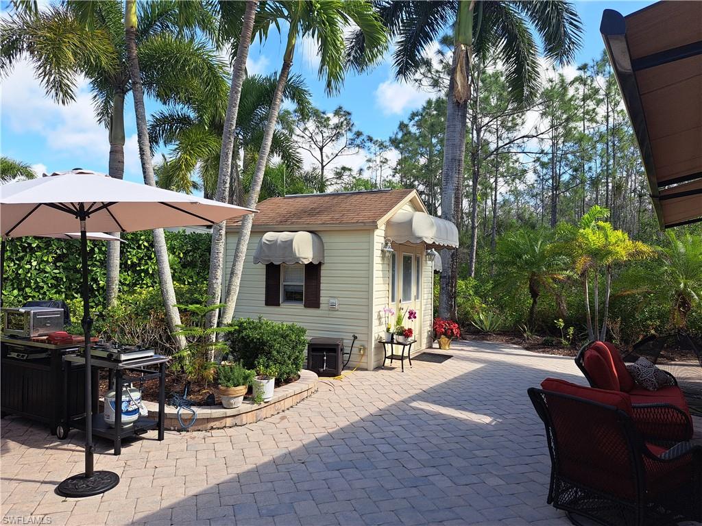 4928 Coach Lane Naples, FL 34114 - Photo 10 of 20 a view of a patio with couches table and chairs under an umbrella with a fire pit and palm trees