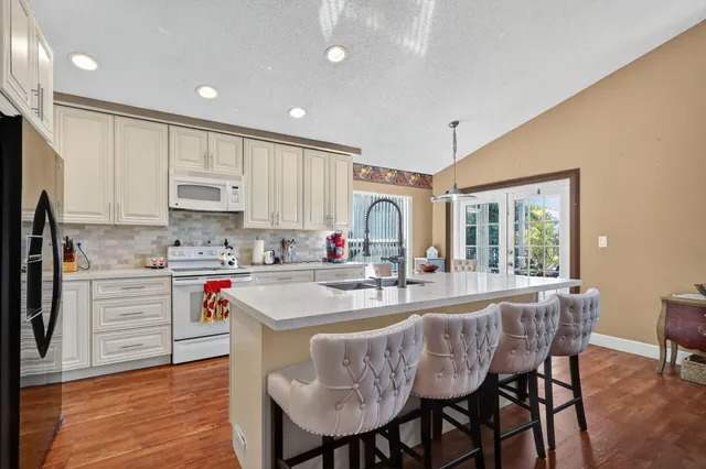 a kitchen with stainless steel appliances granite countertop a stove a sink a refrigerator white cabinets and wooden floor