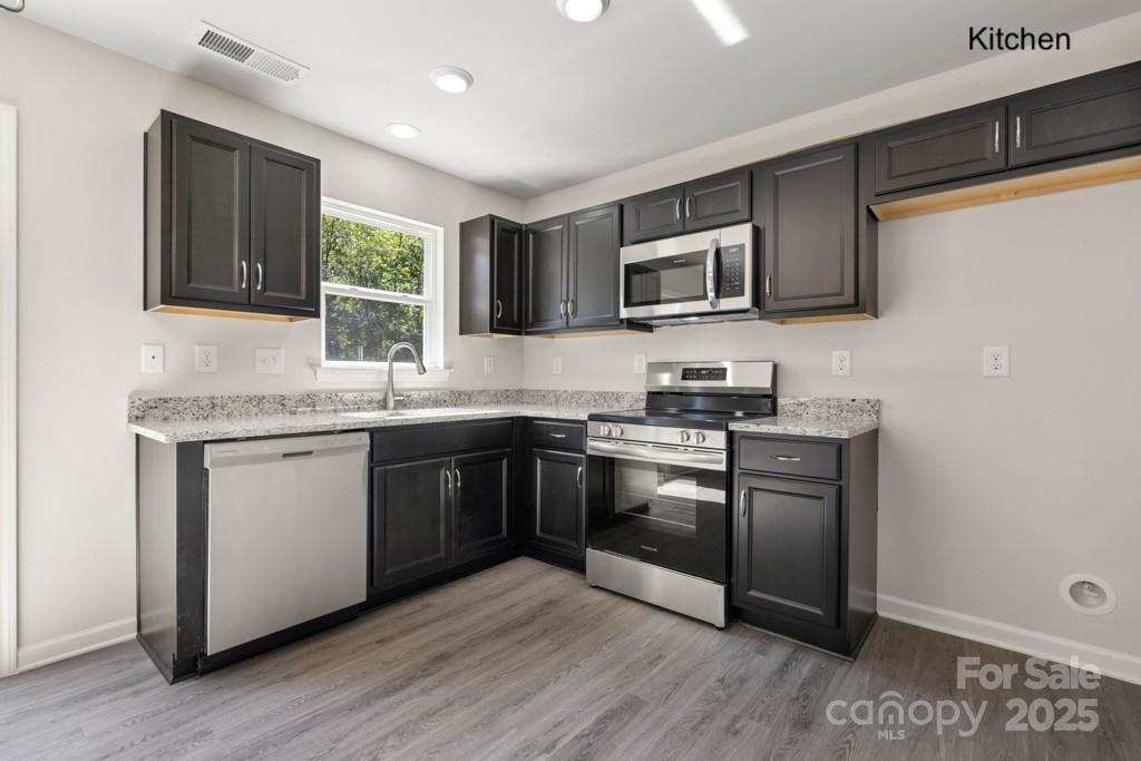 319 Connor Street Lancaster, SC 29720 - Photo 4 of 47 a kitchen with stainless steel appliances granite countertop white cabinets a sink a stove a microwave and wooden floors