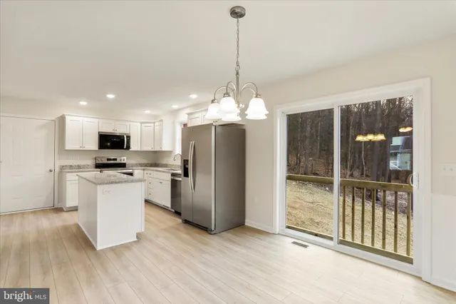 a kitchen with stainless steel appliances kitchen island granite countertop a refrigerator a stove a sink dishwasher a refrigerator and a dining table with wooden floor