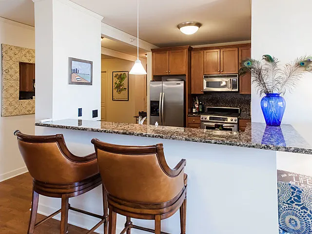 a kitchen with stainless steel appliances granite countertop a dining table chairs refrigerator and sink