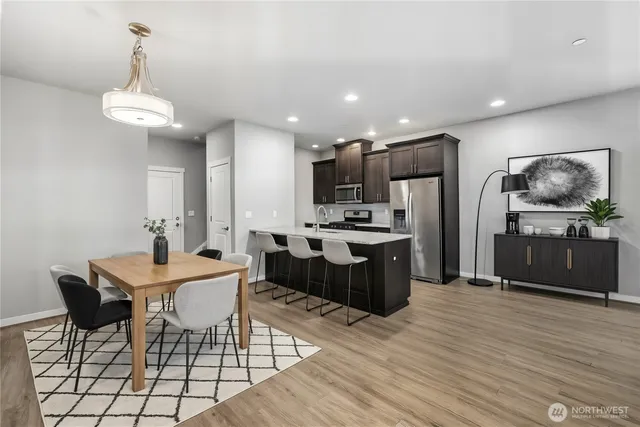 a kitchen with stainless steel appliances kitchen island granite countertop a refrigerator a stove a sink a dining table and chairs with wooden floor
