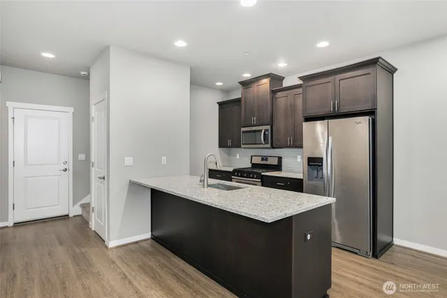 a kitchen with kitchen island granite countertop a refrigerator a sink a stove a microwave and wooden floor