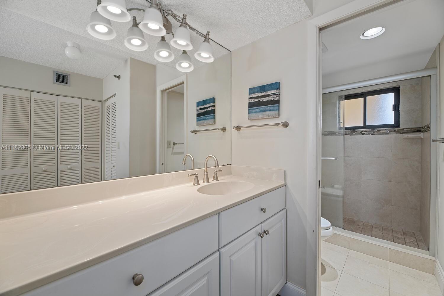 300 Ocean Trail Way, Unit 104 Jupiter, FL 33477 - Photo 11 of 26 a bathroom with a granite countertop sink a large mirror and shower