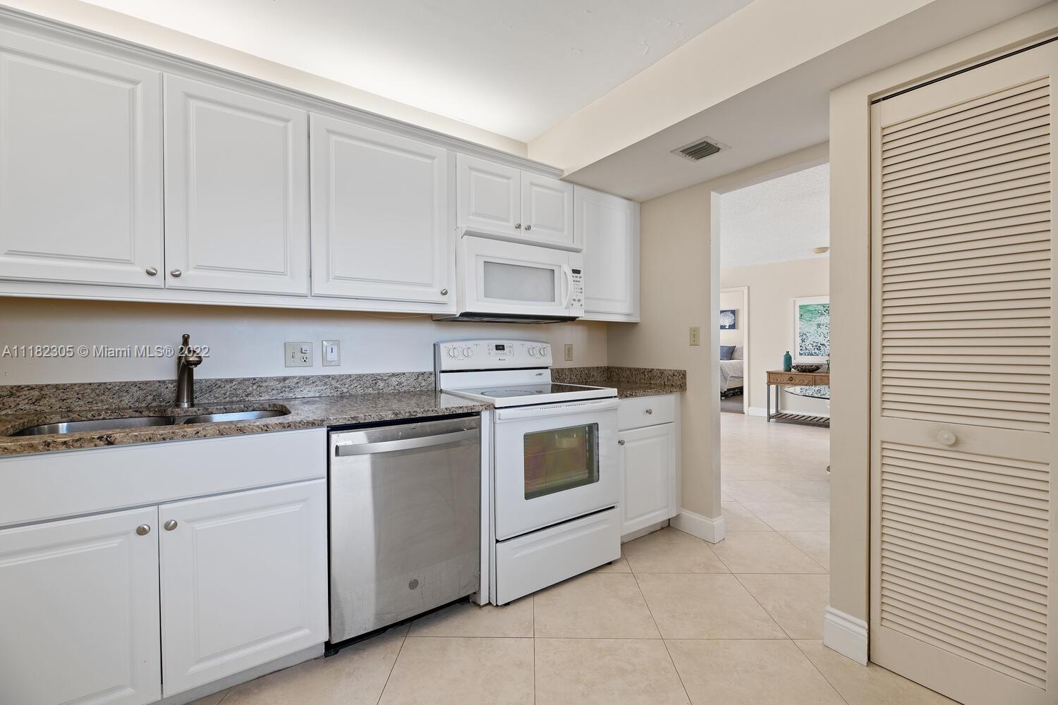 300 Ocean Trail Way, Unit 104 Jupiter, FL 33477 - Photo 6 of 26 a kitchen with granite countertop white cabinets and white appliances