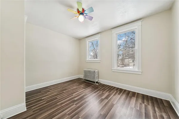 an empty room with wooden floor chandelier fan and windows