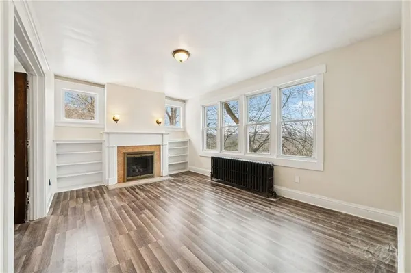 a view of an empty room with wooden floor fireplace and a window