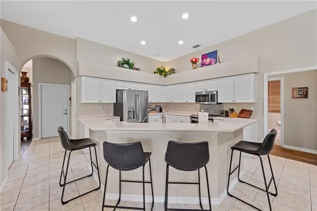 a kitchen with stainless steel appliances kitchen island granite countertop a dining table chairs and a refrigerator