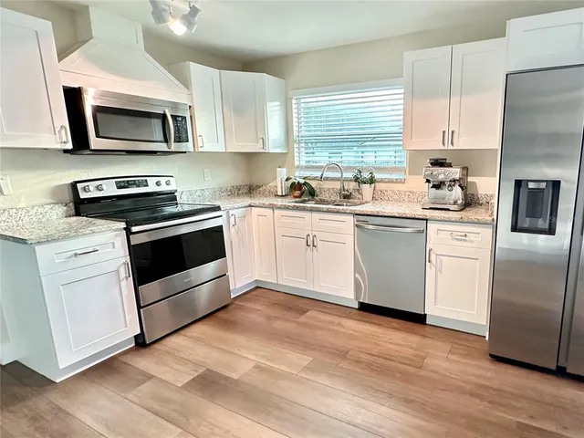 a kitchen with stainless steel appliances granite countertop a stove top oven a sink dishwasher and a refrigerator with wooden floor