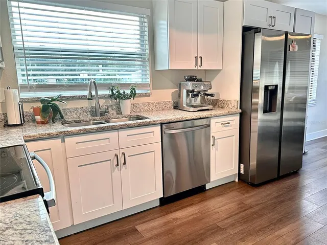 a kitchen with stainless steel appliances granite countertop a refrigerator a sink and white cabinets