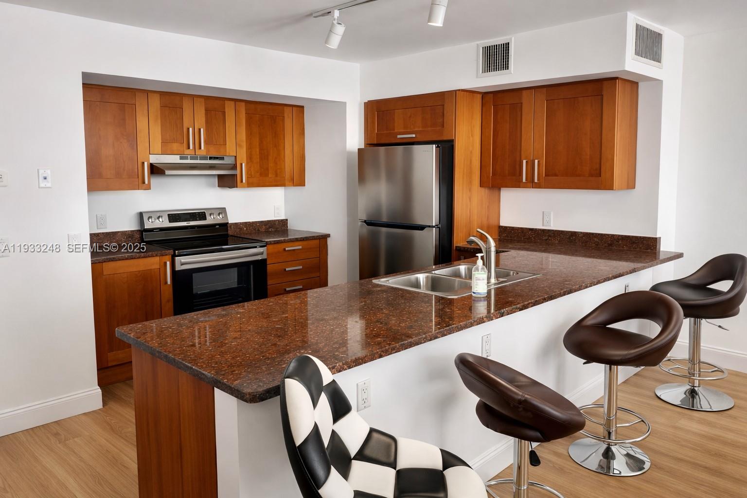 9499 Collins Avenue, Unit 903 Surfside, FL 33154 - Photo 5 of 14 a kitchen with stainless steel appliances granite countertop a stove a refrigerator a sink a dining table and chairs with wooden floor