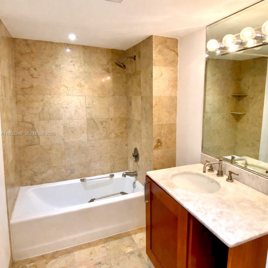 9499 Collins Avenue, Unit 903 Surfside, FL 33154 - Photo 9 of 14 a bathroom with a granite countertop sink a mirror a bathtub and shower