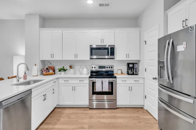 a kitchen with stainless steel appliances a refrigerator a stove a dining table and chairs with wooden floor