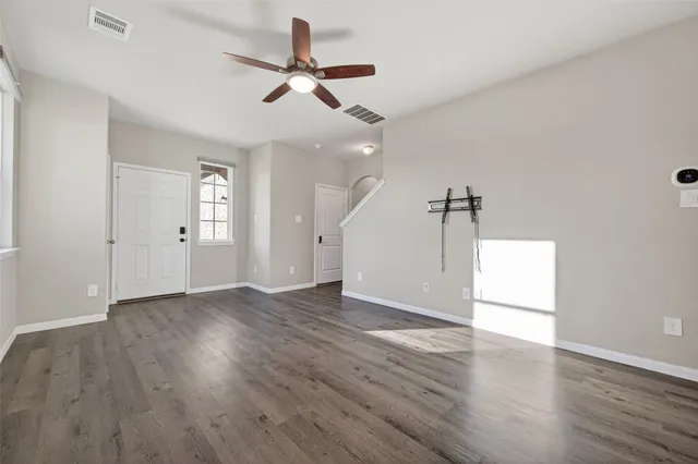an empty room with wooden floor ceiling fan and windows