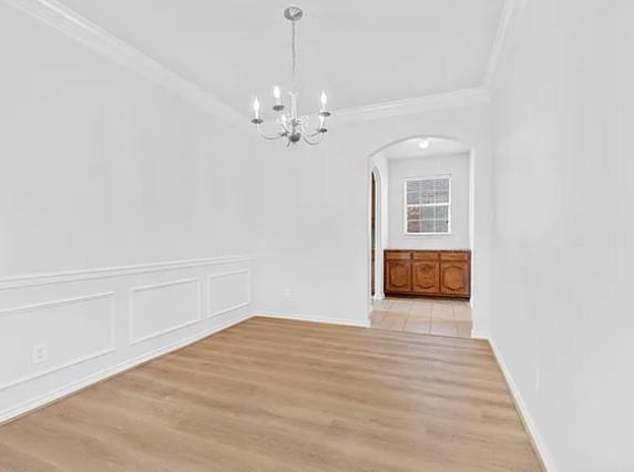 8401 Hitching Trail McKinney, TX 75070 - Photo 16 of 39 Unfurnished dining area with arched walkways, hanging lights, light wood-type flooring, ornamental molding, and a decorative wall