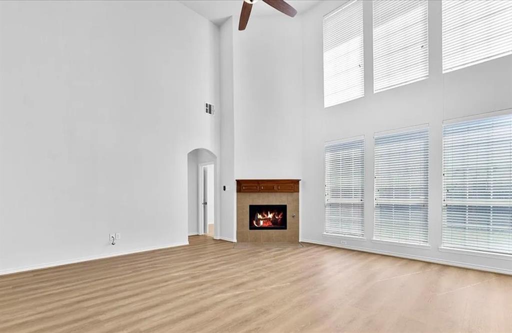 8401 Hitching Trail McKinney, TX 75070 - Photo 26 of 39 Unfurnished living room featuring ceiling fan, arched walkways, a fireplace, light wood-style floors, and a high ceiling